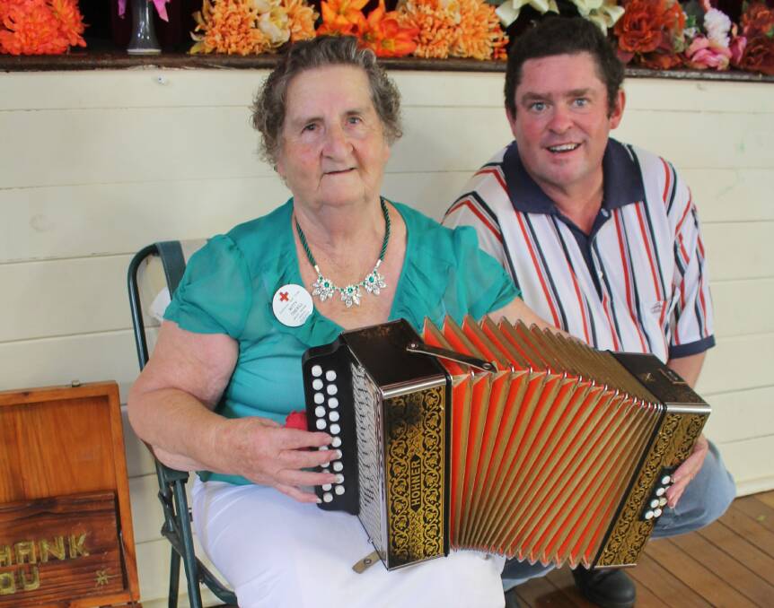Old time skill: Kitty Tisdell of Taree, Mt George Red Cross member, plays a tune on piano accordion as entertainer Peter Manewell of Mt George, looks on at the Tinonee St Patrick’s Day Lunch.