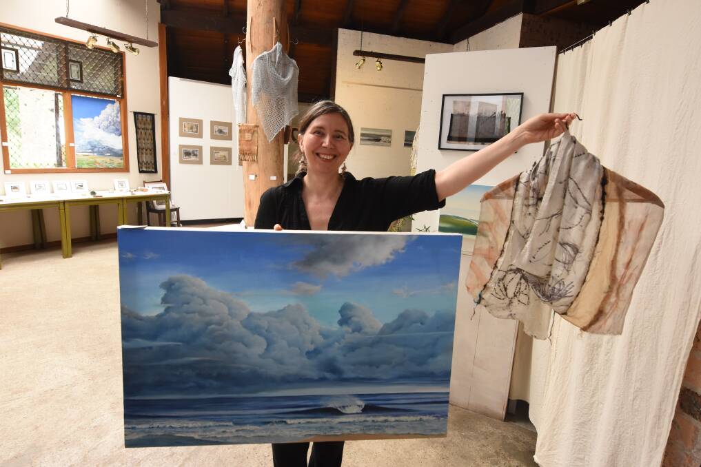 Summer holiday showcase: Jana Pearceova holds a painting by her husband Gerard and one of her textile works. Both are part of the exhibition currently showing at the Green Point Gallery. Photo: Scott Calvin.