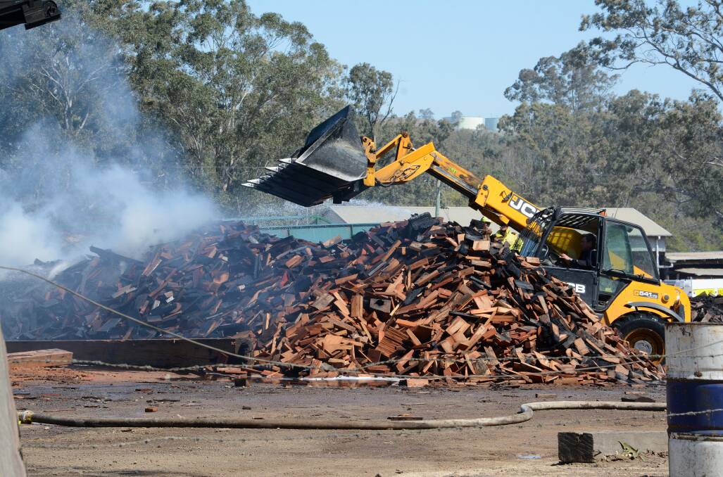 Close call: Excavating equipment moving the still smouldering timber pile on Saturday morning after Friday's fire at Machin's Sawmill. Photo Scott Calvin.