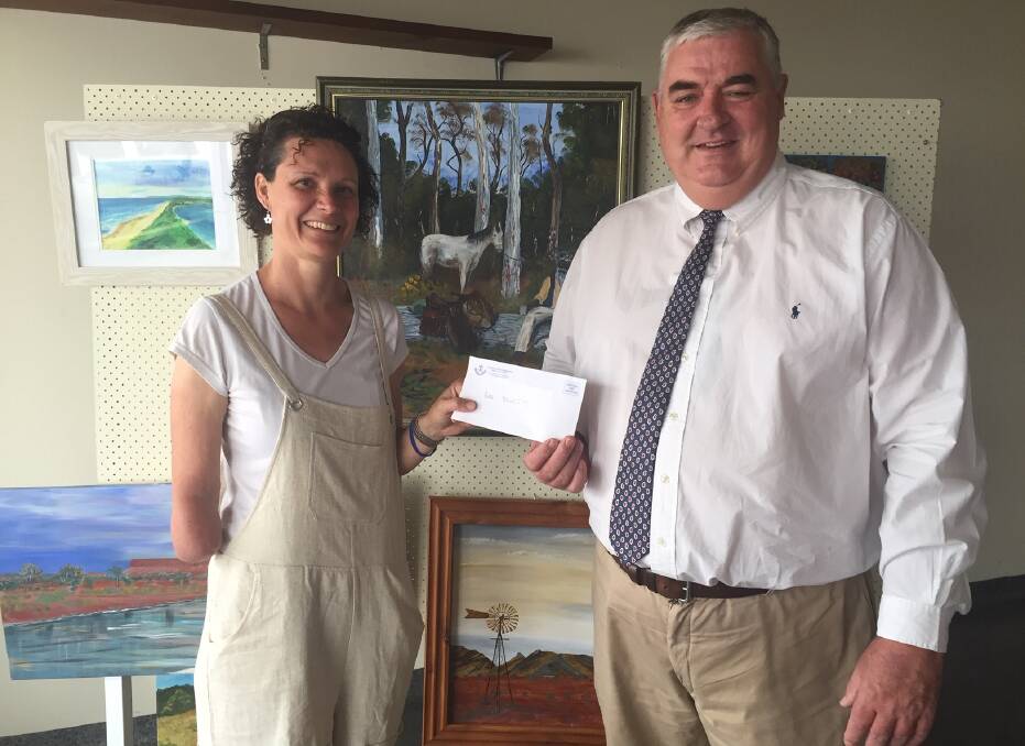 Wingham Memorial Services Club secretary manager Dan McCarthy hands over a cheque to Jillian Oliver of Art and Soul. The paintings behind them were created by veterans who are members of the art therapy group. Photo: Julia Driscoll